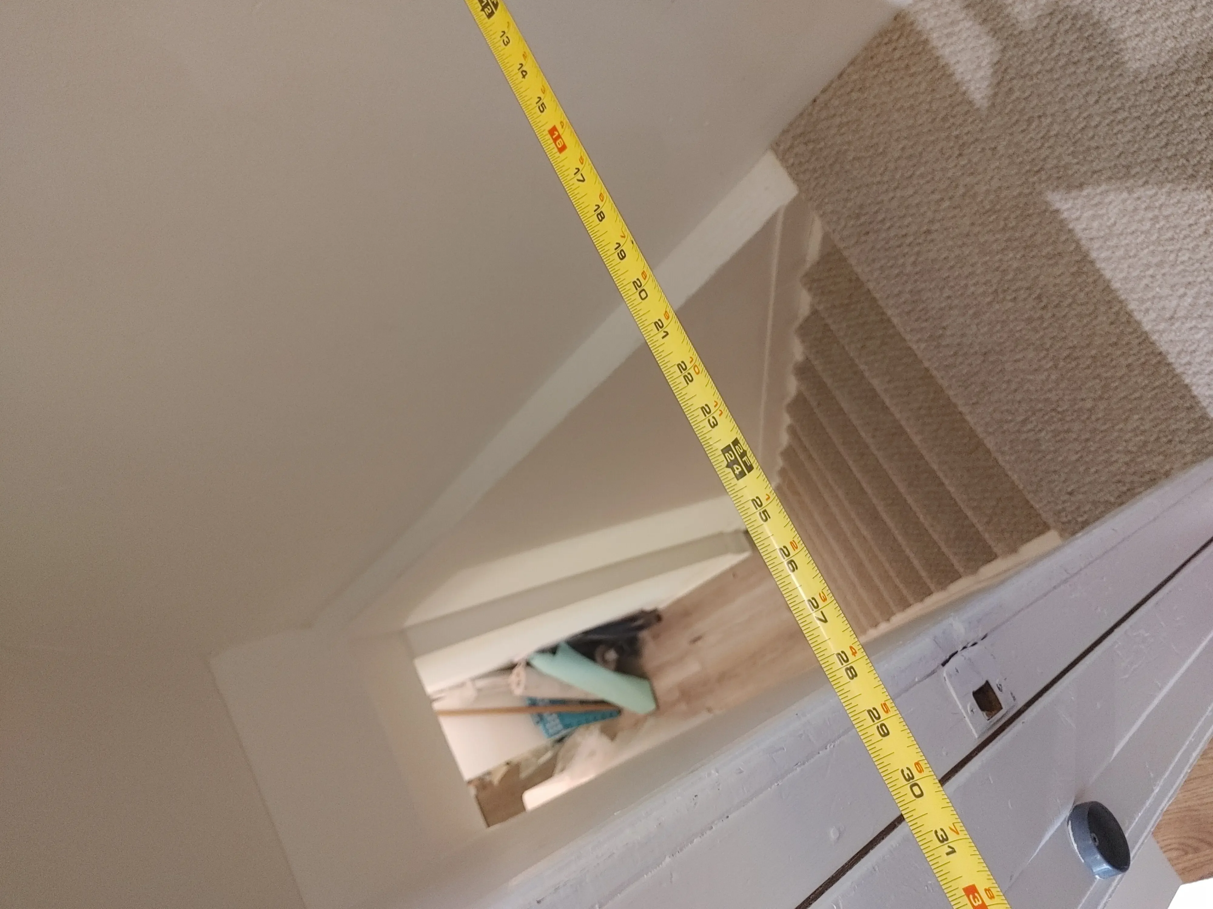 A yellow tape measure stretched across a carpeted staircase landing to gauge clearance and turning room for furniture delivery.